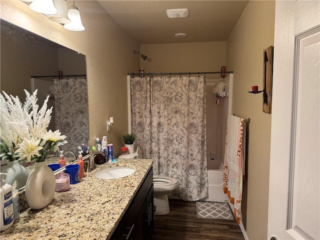 bathroom with vanity, a textured wall, wood finished floors, toilet, and shower / tub combo