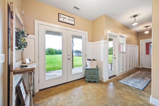 entryway with wainscoting, a decorative wall, concrete floors, french doors, and visible vents