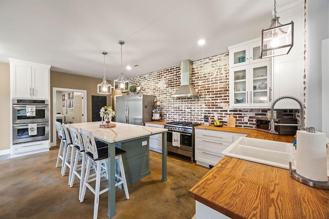 kitchen with wall chimney range hood, stainless steel appliances, concrete flooring, and a sink