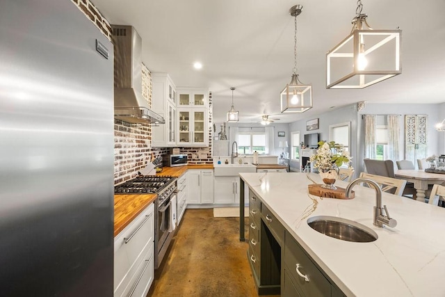 kitchen with stainless steel appliances, a sink, wall chimney exhaust hood, and finished concrete flooring