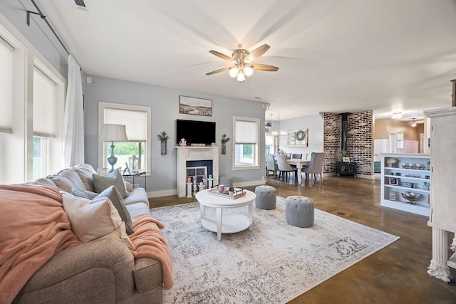 living room featuring finished concrete floors, a wood stove, a ceiling fan, and a healthy amount of sunlight