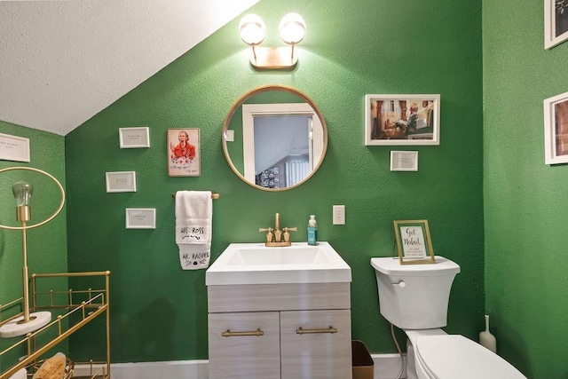 bathroom with a textured wall, vanity, toilet, baseboards, and lofted ceiling