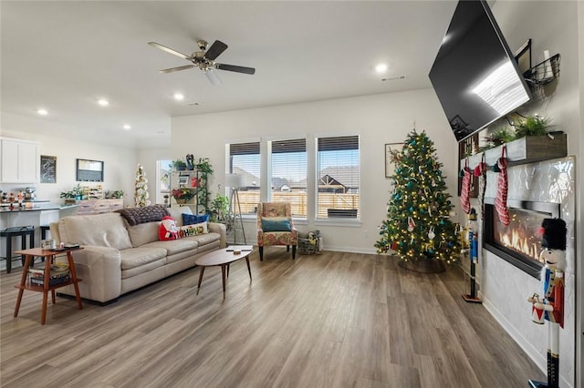 living area featuring a ceiling fan, recessed lighting, baseboards, a tiled fireplace, and wood finished floors