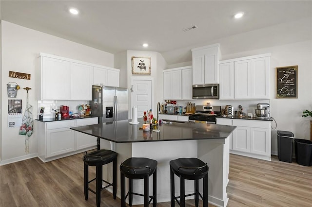kitchen featuring visible vents, a sink, a kitchen breakfast bar, dark countertops, and appliances with stainless steel finishes