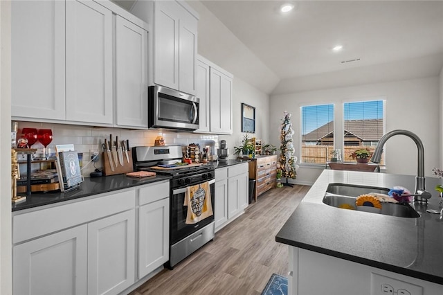 kitchen with a sink, stainless steel appliances, backsplash, dark countertops, and light wood-style floors
