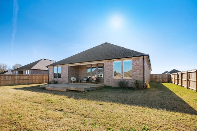 rear view of house featuring a lawn, brick siding, a deck, roof with shingles, and a fenced backyard