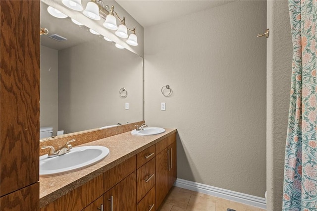 full bathroom with tile patterned flooring, baseboards, double vanity, toilet, and a textured wall