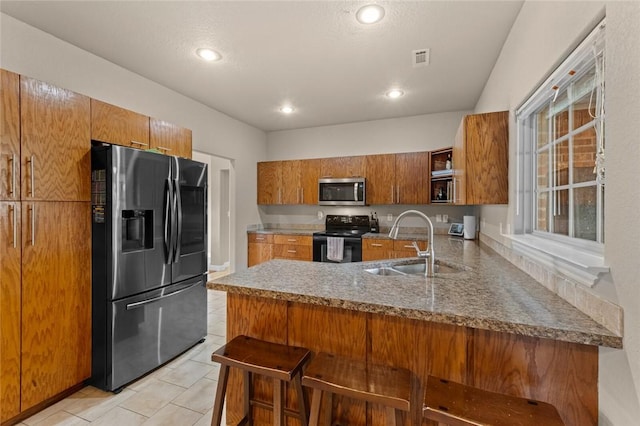kitchen featuring refrigerator with ice dispenser, black electric range, stainless steel microwave, a sink, and brown cabinetry