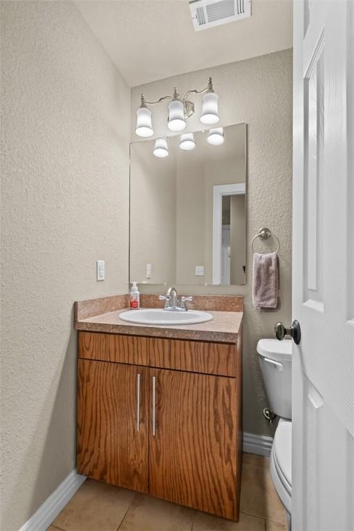 bathroom with a textured wall, tile patterned floors, toilet, vanity, and baseboards