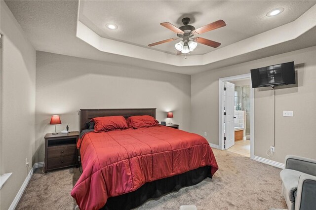 bedroom featuring light colored carpet, a tray ceiling, baseboards, recessed lighting, and ensuite bath