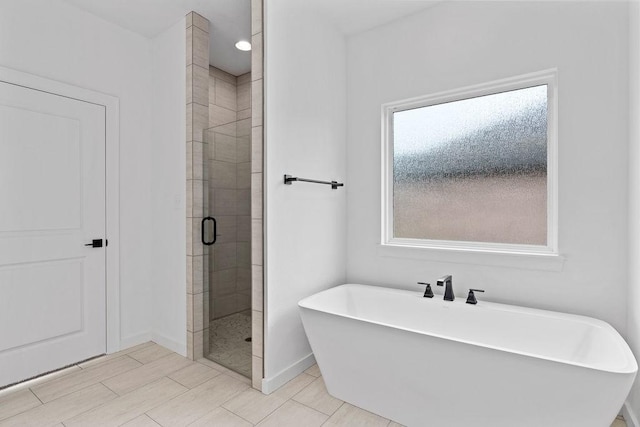 bathroom with a stall shower, a freestanding bath, and baseboards