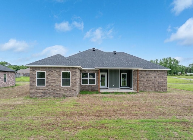 rear view of house with brick siding, roof with shingles, a lawn, and a patio area