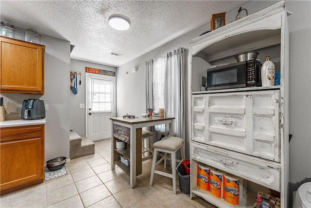 kitchen featuring brown cabinetry, a textured ceiling, visible vents, light countertops, and light tile patterned floors