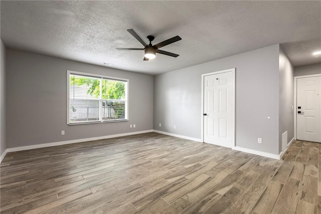 empty room with a ceiling fan, baseboards, a textured ceiling, and wood finished floors