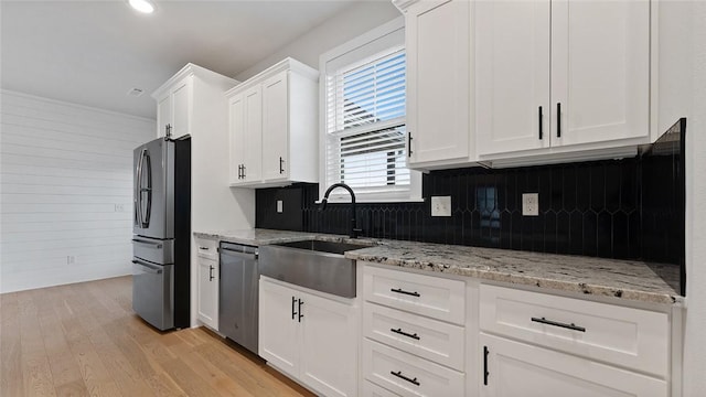 kitchen featuring stainless steel appliances, a sink, white cabinets, backsplash, and light wood-type flooring