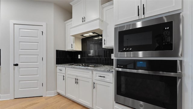 kitchen with appliances with stainless steel finishes, decorative backsplash, light wood-type flooring, white cabinets, and light stone countertops
