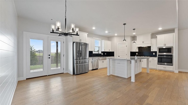 kitchen featuring stainless steel appliances, decorative backsplash, a chandelier, light wood-style floors, and white cabinetry