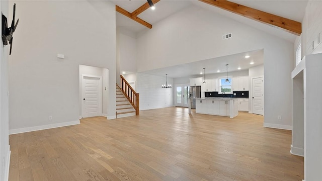 unfurnished living room featuring high vaulted ceiling, stairs, beamed ceiling, light wood-style flooring, and baseboards