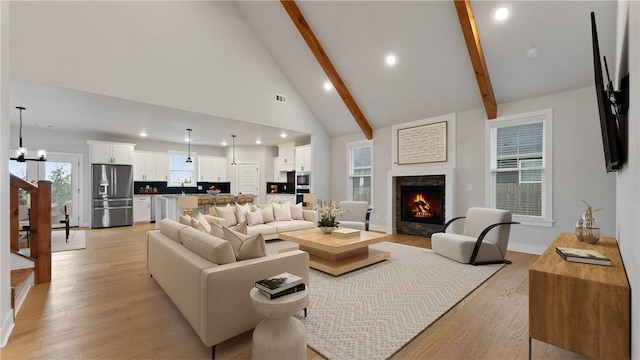 living room with beam ceiling, light wood finished floors, recessed lighting, a lit fireplace, and high vaulted ceiling