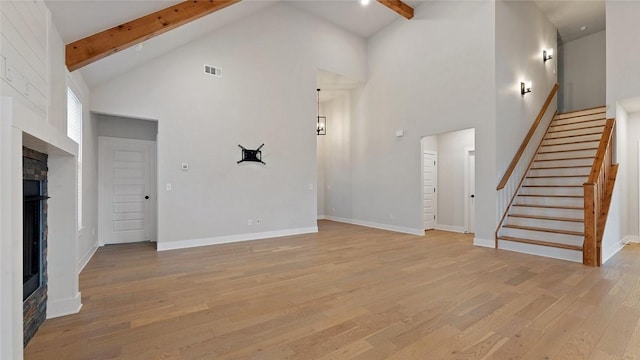 unfurnished living room with high vaulted ceiling, a fireplace, beam ceiling, light wood-style flooring, and stairs