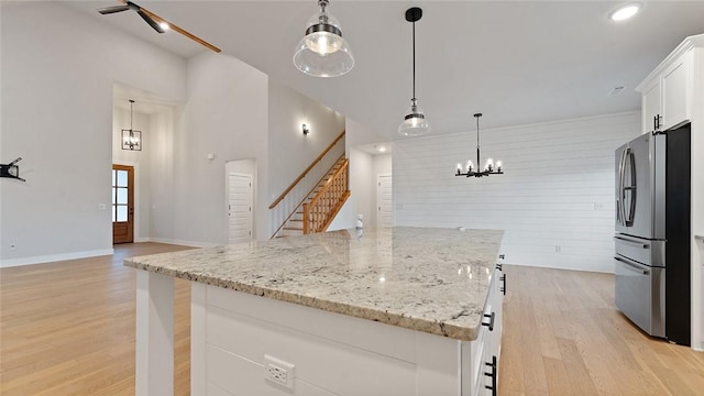 kitchen with freestanding refrigerator, light wood-type flooring, white cabinets, a center island, and light stone countertops