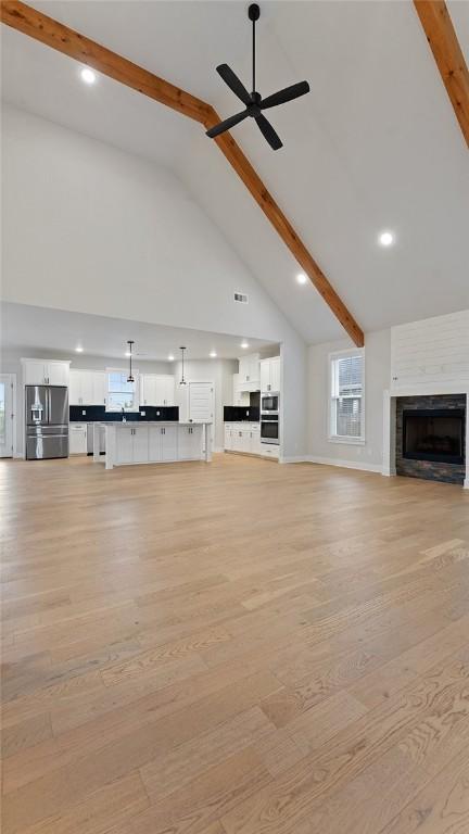 unfurnished living room with beam ceiling, high vaulted ceiling, ceiling fan, light wood-style flooring, and a fireplace