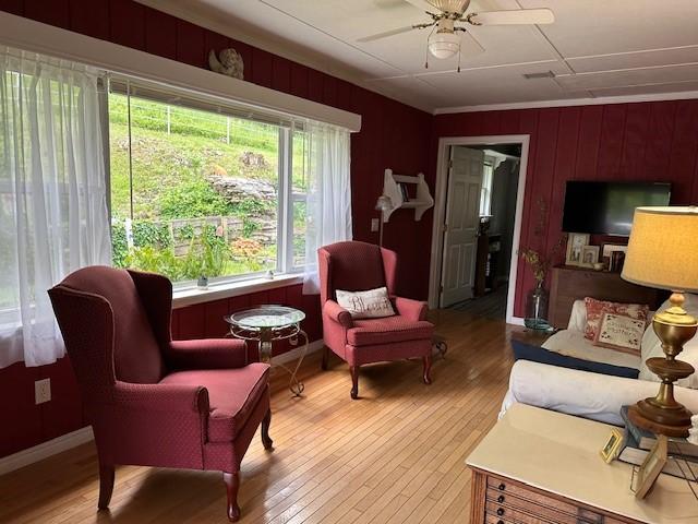 living area featuring light wood-style floors, wood walls, baseboards, and ceiling fan