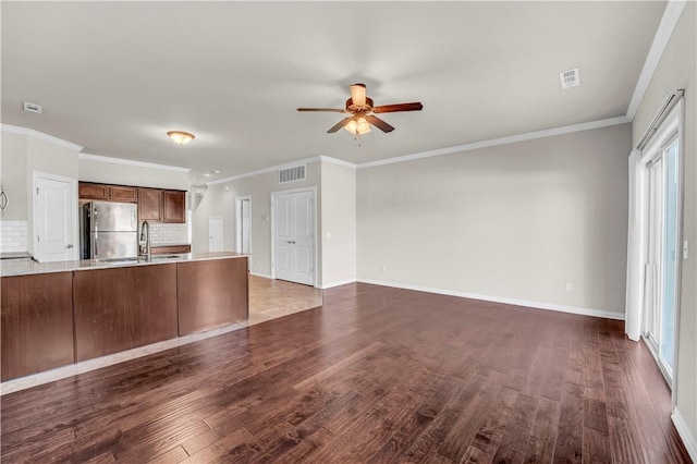 unfurnished living room featuring a sink, crown molding, visible vents, ceiling fan, and dark wood-style floors