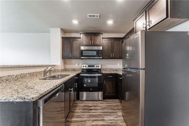 kitchen with a sink, stainless steel appliances, wood finished floors, visible vents, and dark brown cabinetry