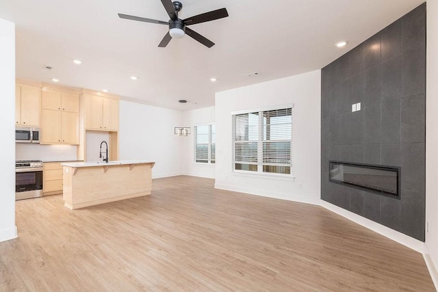 unfurnished living room featuring recessed lighting, baseboards, ceiling fan, a fireplace, and light wood-type flooring