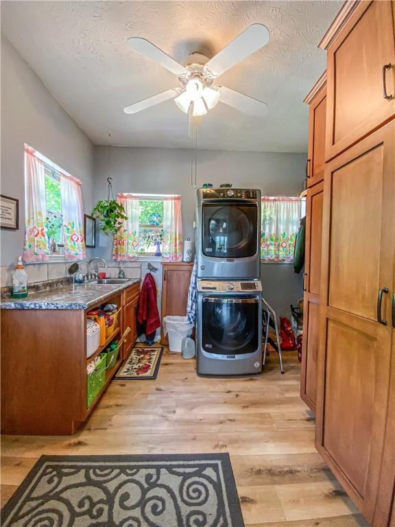 laundry room with a ceiling fan, a sink, stacked washer and dryer, a textured ceiling, and light wood-style floors
