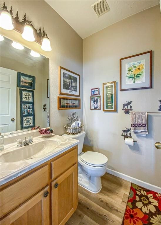 bathroom with toilet, wood finished floors, vanity, visible vents, and baseboards