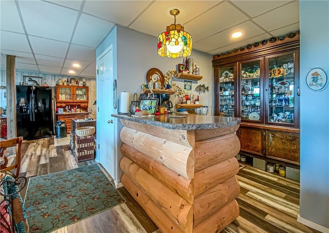 bar featuring decorative light fixtures, black fridge with ice dispenser, dark wood-type flooring, and a drop ceiling
