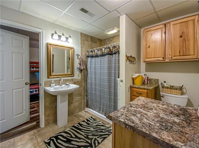 bathroom featuring a tile shower, a drop ceiling, tile walls, and visible vents