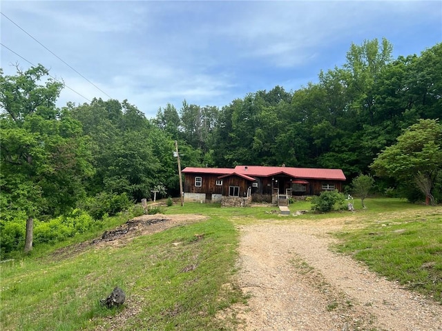 view of front of property with dirt driveway and a forest view