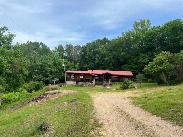 view of front of house featuring a forest view, driveway, and metal roof