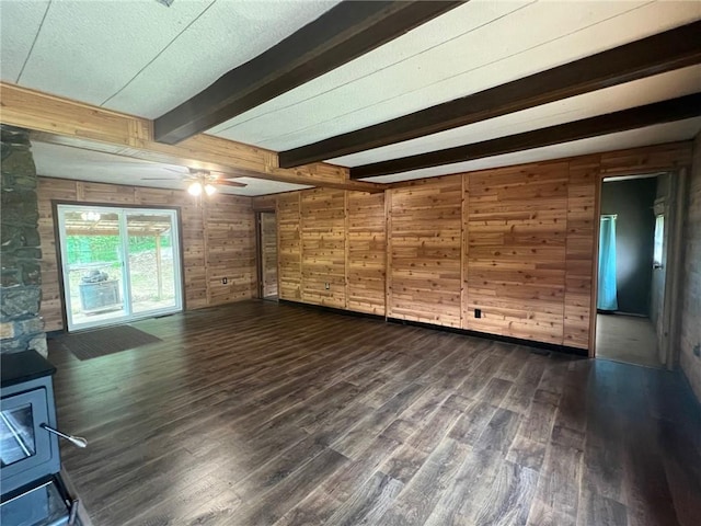 interior space with a ceiling fan, beam ceiling, a wood stove, wooden walls, and dark wood-style floors