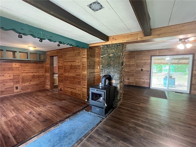 unfurnished living room with a wood stove, beam ceiling, wooden walls, and wood finished floors