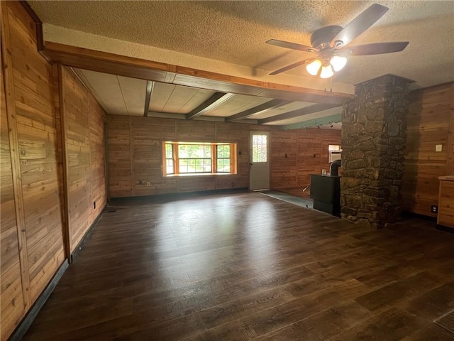 unfurnished living room featuring beam ceiling, a textured ceiling, ceiling fan, wooden walls, and wood-type flooring