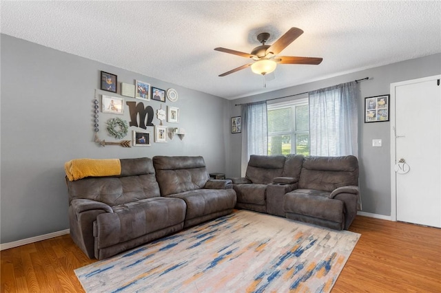 living area with a textured ceiling, baseboards, a ceiling fan, and wood finished floors