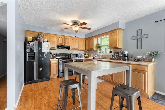 kitchen with light wood-type flooring, ceiling fan, black appliances, under cabinet range hood, and light countertops