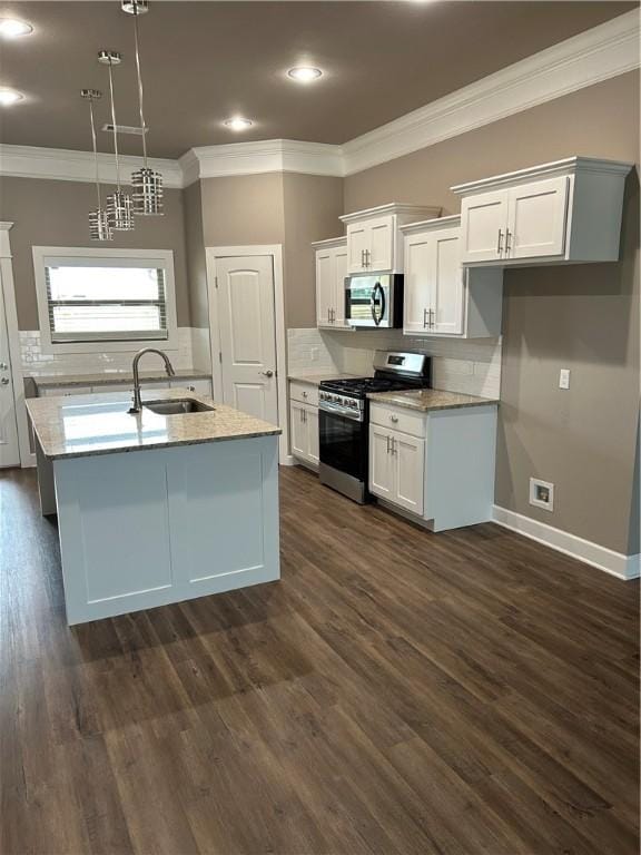 kitchen featuring appliances with stainless steel finishes, a sink, ornamental molding, white cabinetry, and a center island with sink