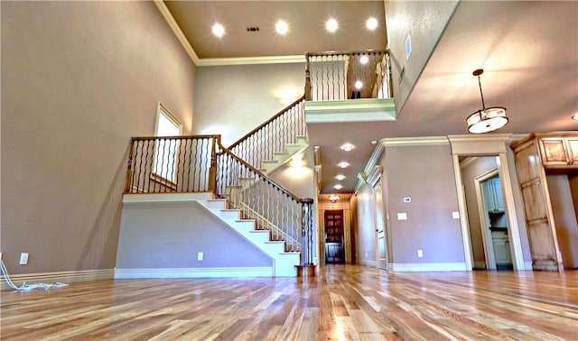 stairs with baseboards, ornamental molding, visible vents, wood finished floors, and a high ceiling