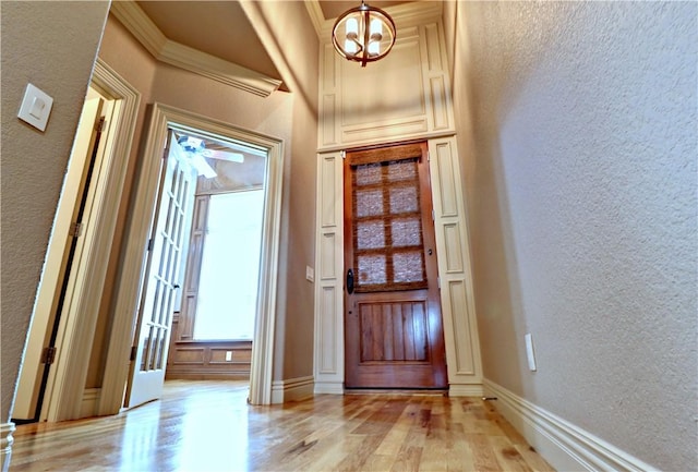 foyer entrance with light wood finished floors, a textured wall, baseboards, and an inviting chandelier