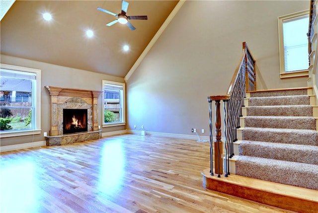 unfurnished living room with wood finished floors, high vaulted ceiling, stairway, baseboards, and ceiling fan