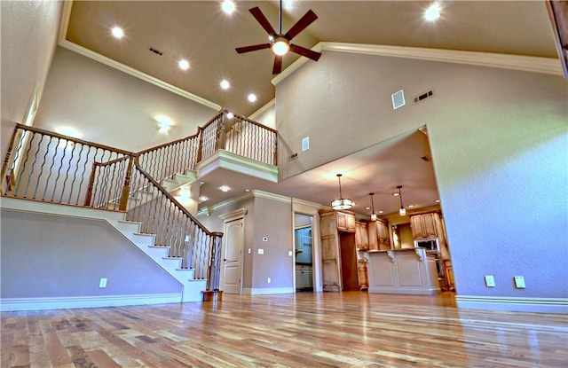 unfurnished living room with crown molding, stairs, light wood-type flooring, and ceiling fan