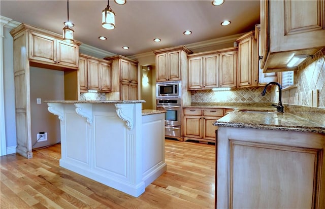 kitchen featuring a breakfast bar area, a sink, appliances with stainless steel finishes, light stone counters, and ornamental molding