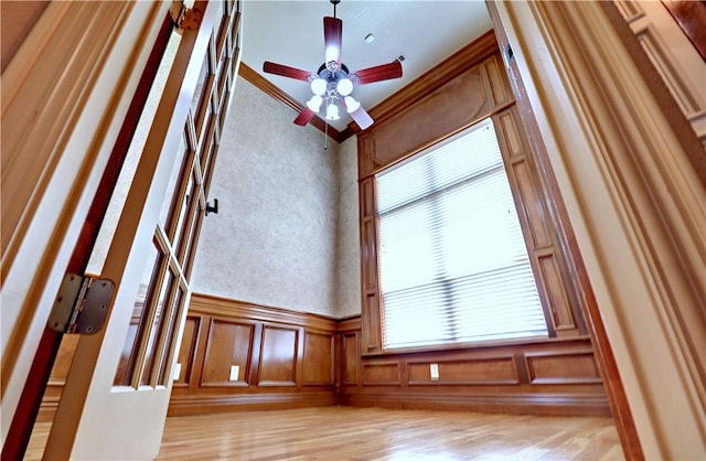 unfurnished room with light wood-type flooring, wainscoting, and ceiling fan