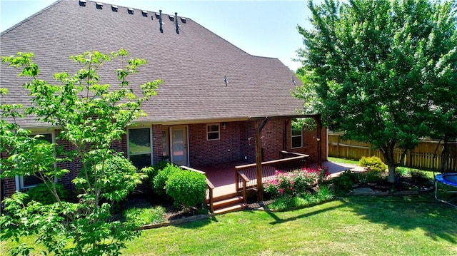 rear view of house featuring fence, a deck, brick siding, a lawn, and a shingled roof