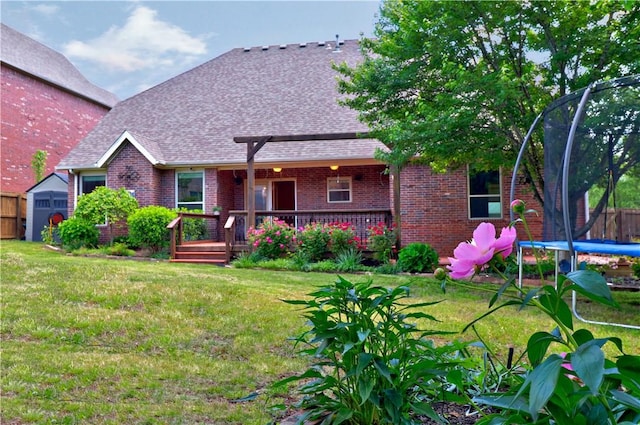 view of front of property featuring fence, a trampoline, brick siding, a wooden deck, and a front lawn